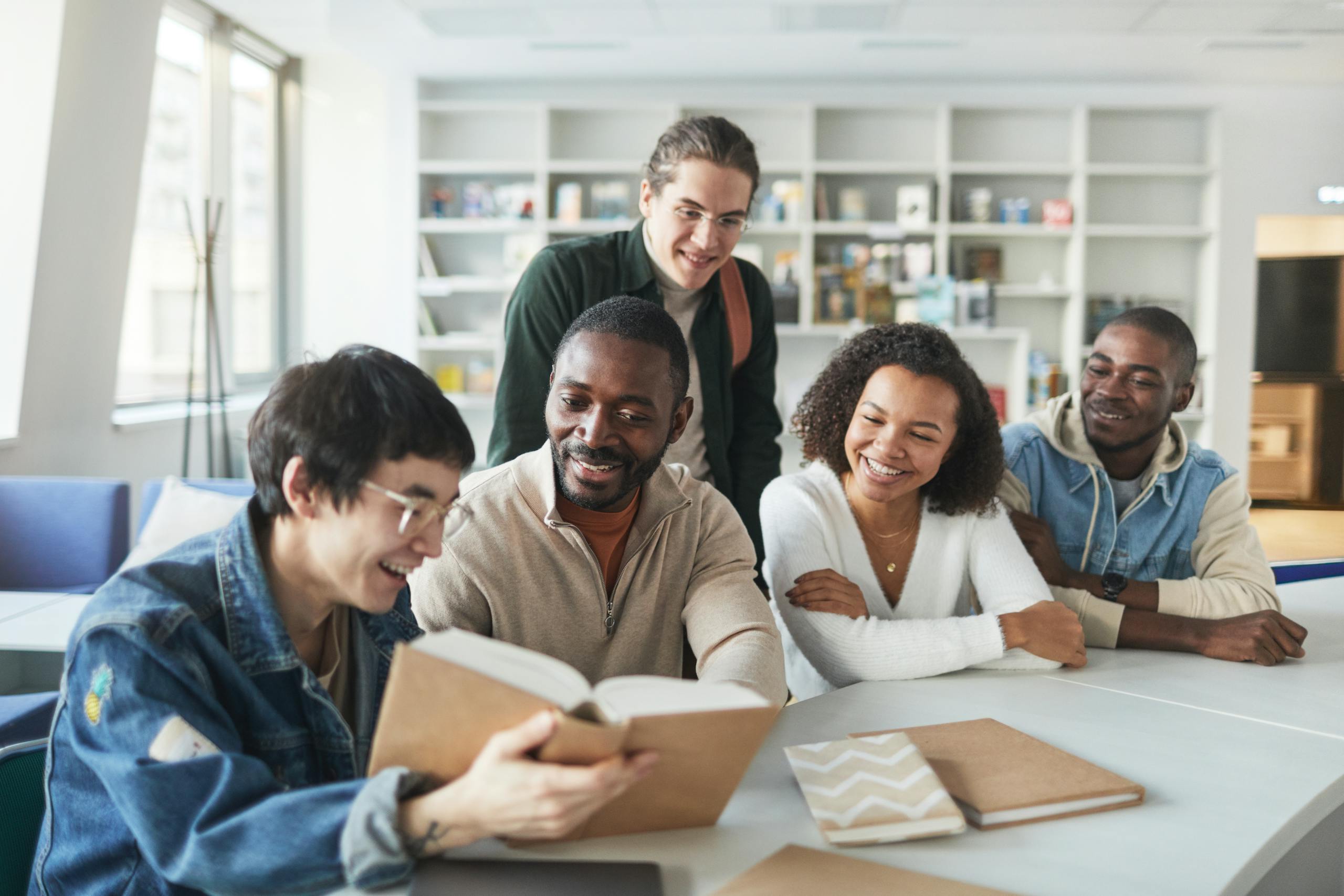 A group of diverse students smiling and studying together indoors in a library setting.
