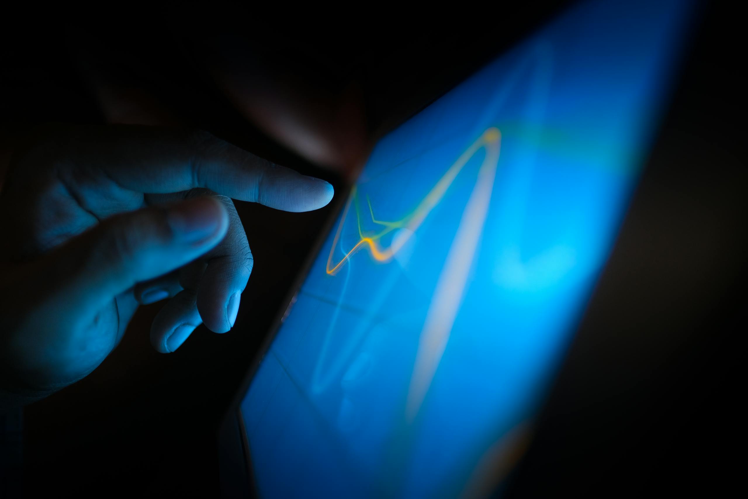Close-up of a hand interacting with a touchscreen displaying dynamic graphs.